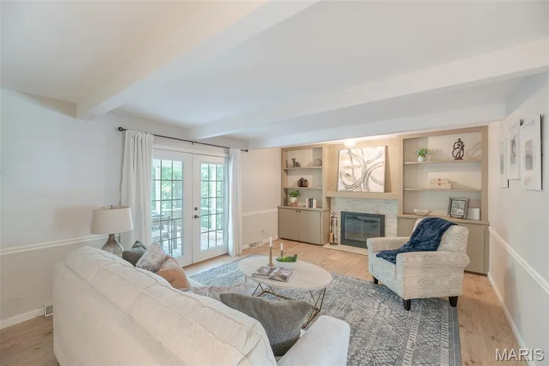 Bright, light-filled living room featuring hardwood flooring, built-in cabinetry with shelving and fireplace surround, and French doors leading to outdoor space — 1526 Candish Lane, Chesterfield, MO 63017
