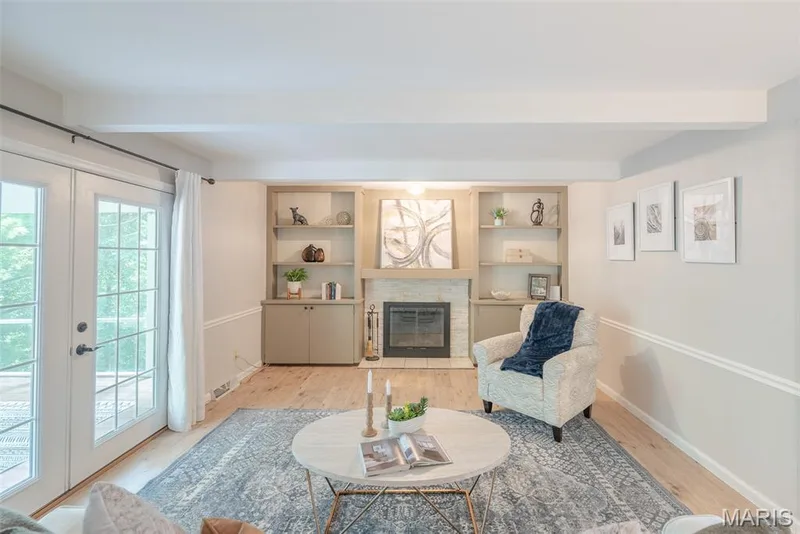 Bright and airy living room featuring hardwood flooring, built-in cabinetry with display shelving and fireplace surround, recessed ceiling lighting, and glass French doors providing natural light — 1526 Candish Lane, Chesterfield, MO 63017