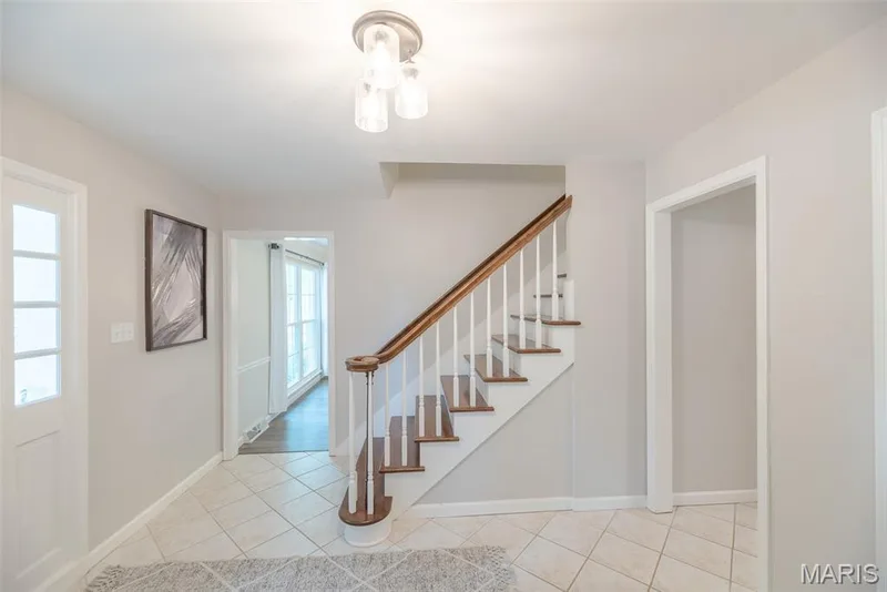 Tiled flooring, wood staircase with white risers, wood handrail, and a modern ceiling light fixture — 1526 Candish Lane, Chesterfield, MO 63017