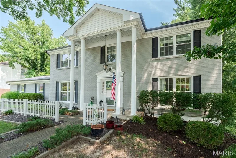 Two-story brick exterior with a columned portico, black shutters, white window trim, and a picket fence — 1526 Candish Lane, Chesterfield, MO 63017