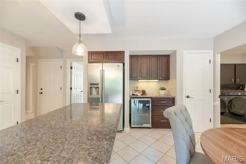 Expansive island with a speckled countertop, stainless steel refrigerator, dark wood cabinetry, beverage refrigerator, and white tile flooring — 1526 Candish Lane, Chesterfield, MO 63017