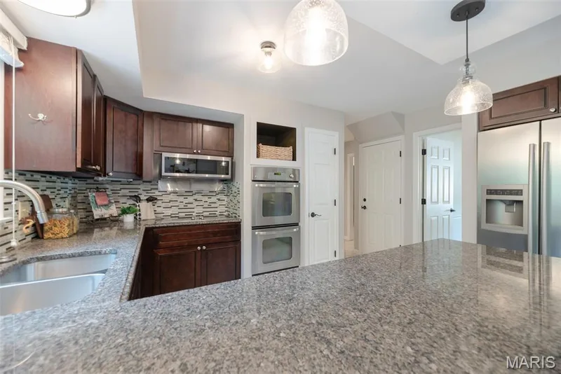 Kitchen featuring an island with a speckled countertop, dark wood-finish cabinetry, stainless steel double ovens, a stainless steel refrigerator, and pendant lighting — 1526 Candish Lane, Chesterfield, MO 63017