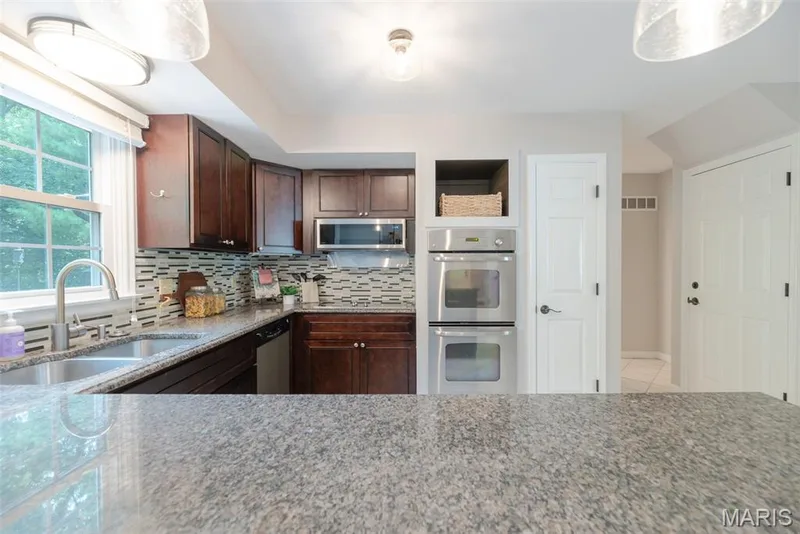 Kitchen featuring dark wood cabinetry, stainless steel appliances, a tile backsplash, and stone countertops — 1526 Candish Lane, Chesterfield, MO 63017