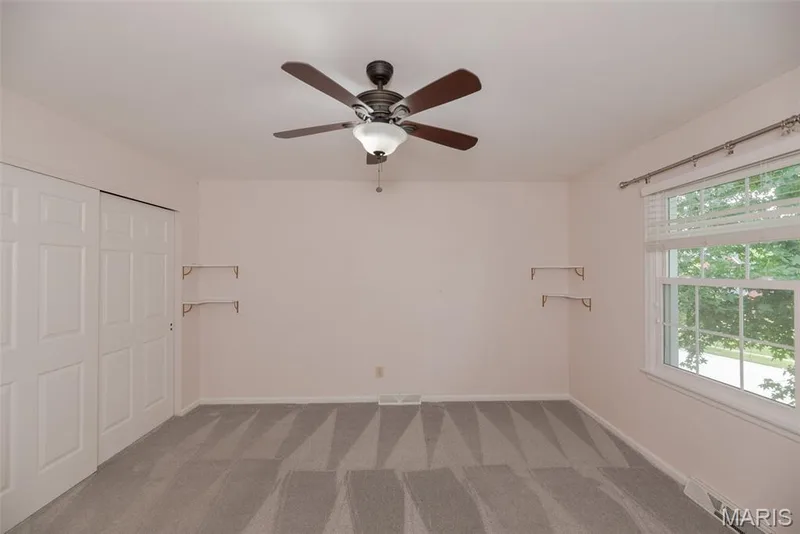 Wall-to-wall carpeting with a geometric pattern, ceiling fan with integrated lighting, window with blinds, and white bi-fold closet doors — 1526 Candish Lane, Chesterfield, MO 63017