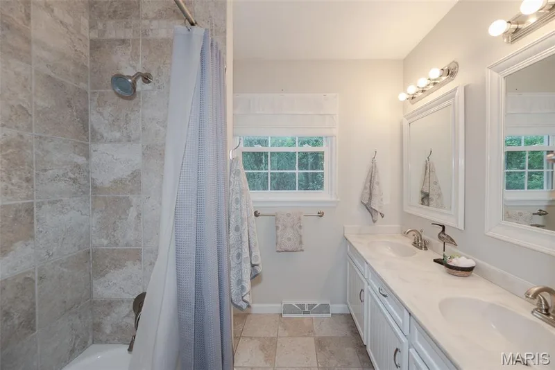 Dual vanity with undermount sinks and brushed nickel faucets, framed mirrors with sconce lighting, tiled flooring, and a tiled shower surround — 1526 Candish Lane, Chesterfield, MO 63017