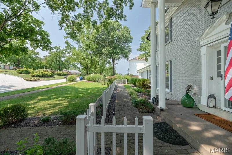 Brick facade with classic white columns, an inviting front porch, and a white picket fence bordering a brick pathway — 1526 Candish Lane, Chesterfield, MO 63017