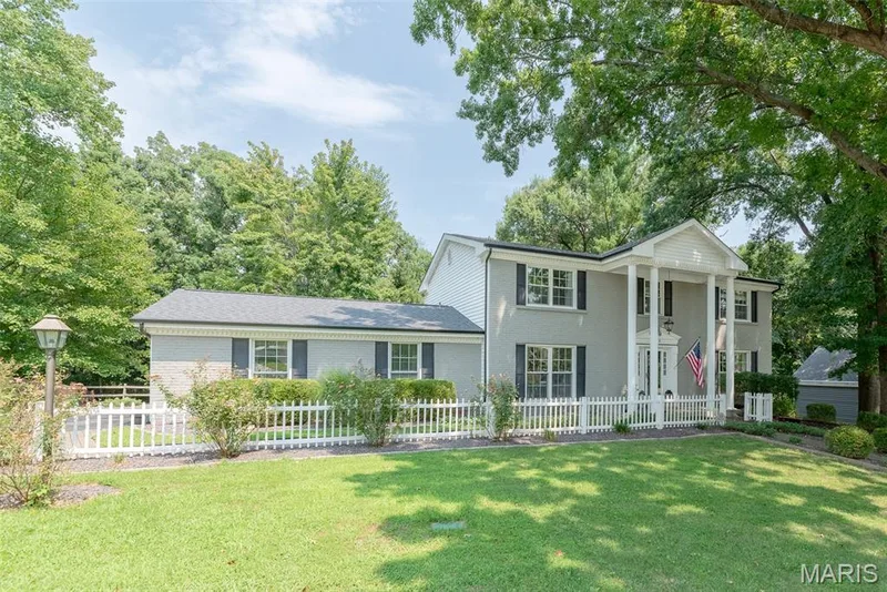 Traditional exterior with a columned portico, brick facade, white picket fence, mature trees, and a manicured lawn — 1526 Candish Lane, Chesterfield, MO 63017