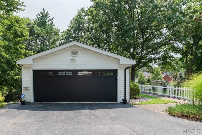 Attached garage with a black garage door and upper window panels, white siding, and a decorative gable vent — 1526 Candish Lane, Chesterfield, MO 63017