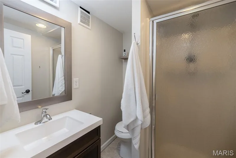 Vanity with integrated sink, chrome faucet, framed mirror, and enclosed shower with textured glass — 1526 Candish Lane, Chesterfield, MO 63017