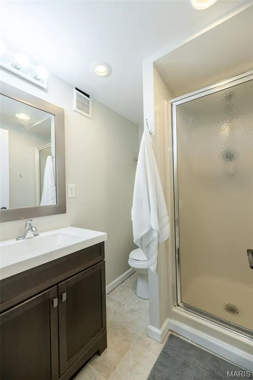 Vanity with a white countertop and wood-finish cabinetry, frameless mirror, recessed lighting, and a shower with a frosted glass enclosure — 1526 Candish Lane, Chesterfield, MO 63017
