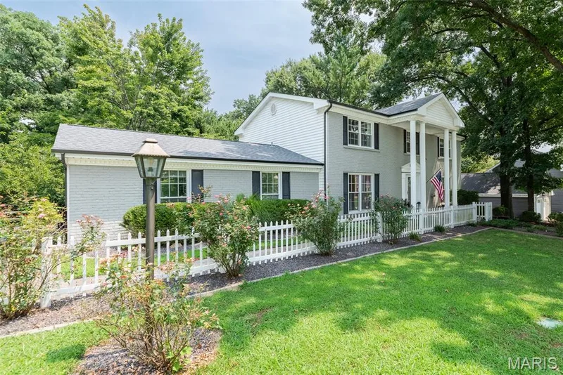 Classic Colonial-style home featuring white horizontal siding, black shutters, and a covered front porch with white railings — 1526 Candish Lane, Chesterfield, MO 63017