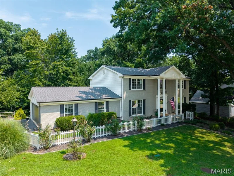 Two-story exterior with a portico entry featuring four columns, a white picket fence, a manicured lawn, and mature trees — 1526 Candish Lane, Chesterfield, MO 63017