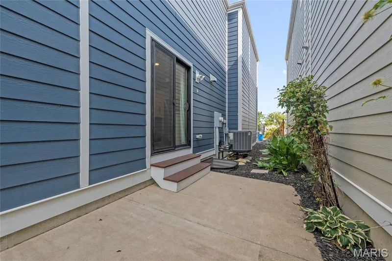 Sliding glass door entry to a concrete patio bordered by a landscaped area with dark mulch and stepping stones — 3429 Sublette Street, St Charles, MO 63301