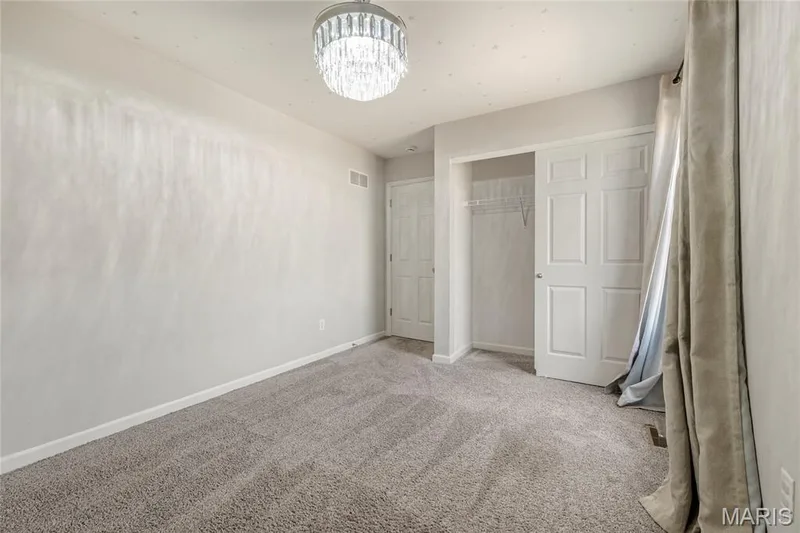 Neutral-toned room featuring a decorative crystal chandelier, light gray carpeting, white baseboards, and a white six-panel closet door — 3429 Sublette Street, St Charles, MO 63301