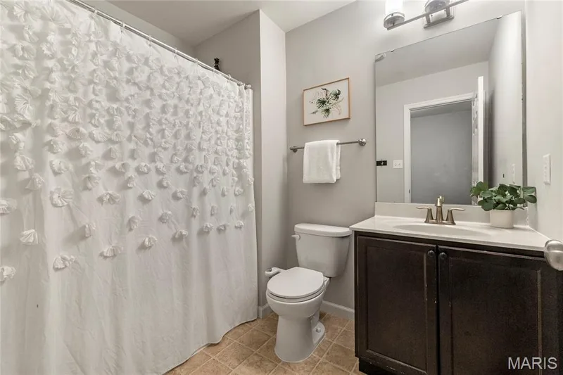 Full bathroom featuring a dark wood-finish vanity with an integrated sink, a large wall-mounted mirror, a standard toilet, and tiled flooring — 3429 Sublette Street, St Charles, MO 63301