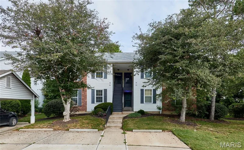 Two-story building with white siding, dark shutters, a front staircase, and mature trees — 146 Old Buggy Court #A, St Charles, MO 63304