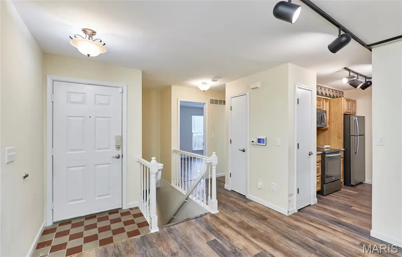 Entryway with checkerboard tile flooring, leading to a kitchen featuring wood-finish cabinetry, stainless steel appliances, and track lighting — 146 Old Buggy Court #A, St Charles, MO 63304