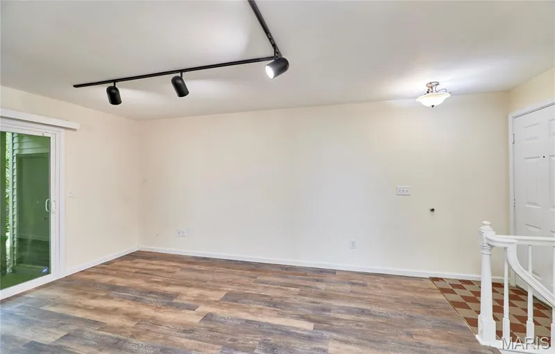 Wood-finish flooring, sliding glass door, overhead track lighting, flush mount ceiling light, and a staircase with a white banister — 146 Old Buggy Court #A, St Charles, MO 63304