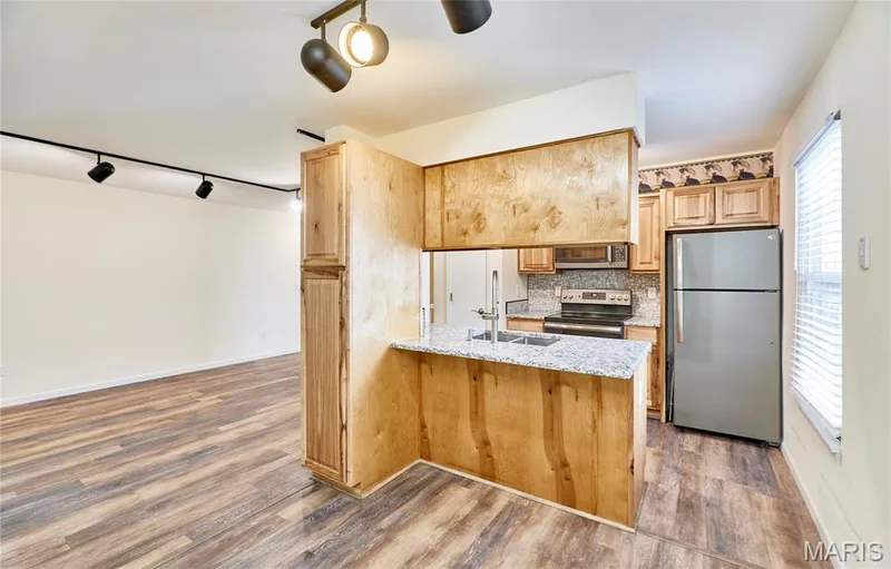 Kitchen with wood-finish cabinetry, stainless steel appliances, granite countertops, and tile backsplash — 146 Old Buggy Court #A, St Charles, MO 63304