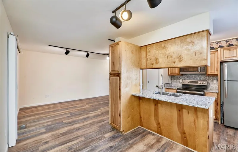 Wood-finish flooring throughout, track lighting, kitchen with wood cabinetry, granite-style countertops, and a stainless steel refrigerator — 146 Old Buggy Court #A, St Charles, MO 63304