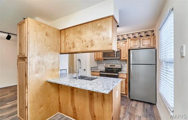 Kitchen featuring wood cabinetry, stainless steel appliances, granite-style countertops, mosaic tile backsplash, and wood-finish flooring — 146 Old Buggy Court #A, St Charles, MO 63304