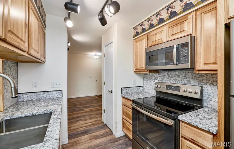 Kitchen featuring wood cabinetry, granite-finish countertops, and a mosaic tile backsplash — 146 Old Buggy Court #A, St Charles, MO 63304