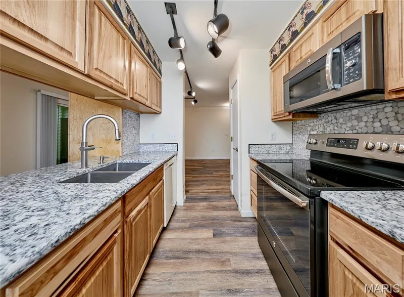 Kitchen featuring wood cabinetry, light-toned countertops, stainless steel appliances, and wood-finish flooring — 146 Old Buggy Court #A, St Charles, MO 63304