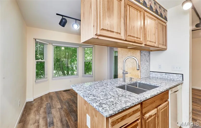Wood-finish flooring, bay window, granite-style countertops, double basin sink with gooseneck faucet, and natural wood cabinetry — 146 Old Buggy Court #A, St Charles, MO 63304