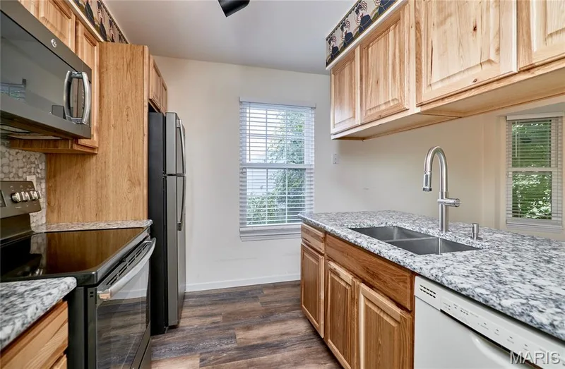 Kitchen featuring wood-finish cabinetry, speckled countertops, stainless steel appliances, and a double basin sink with a gooseneck faucet — 146 Old Buggy Court #A, St Charles, MO 63304