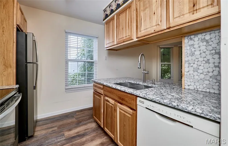 Wood-finish flooring, wood cabinetry, stone-finish countertops, stainless steel appliances, and a double basin sink — 146 Old Buggy Court #A, St Charles, MO 63304