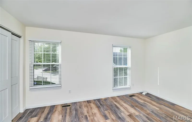 Wood-finish flooring, white walls, two windows with blinds, and white sliding closet doors — 146 Old Buggy Court #A, St Charles, MO 63304