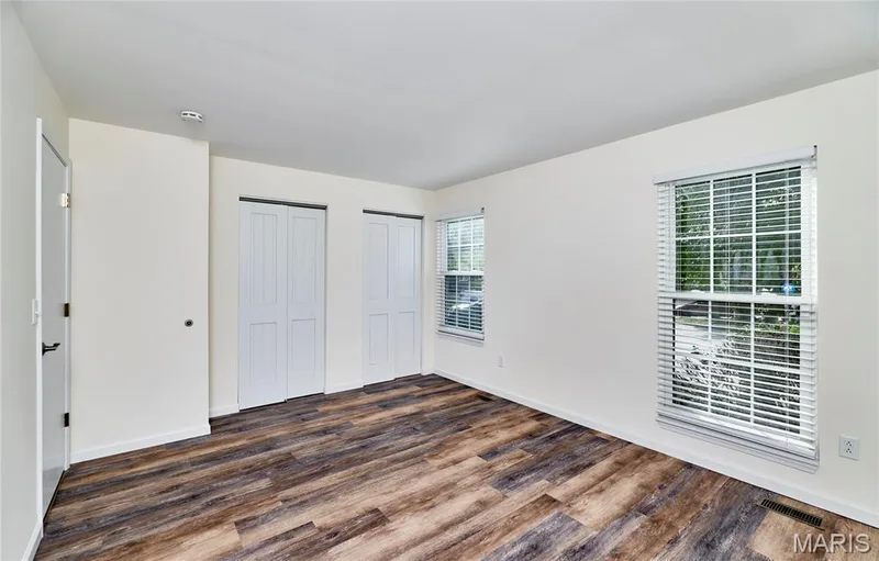 Wood-finish flooring, two windows with blinds, two bi-fold closet doors, and white walls — 146 Old Buggy Court #A, St Charles, MO 63304