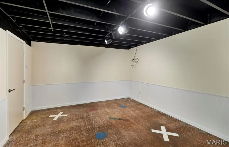Lower level family room with exposed black ceiling joists, track lighting, light-toned walls, white wainscoting, and a light-colored door with dark hardware — 146 Old Buggy Court #A, St Charles, MO 63304