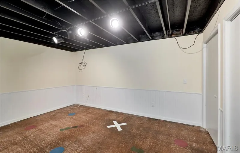 Lower level family room with track lighting, exposed ceiling joists, neutral wall paint, white wainscoting, and a white interior door — 146 Old Buggy Court #A, St Charles, MO 63304