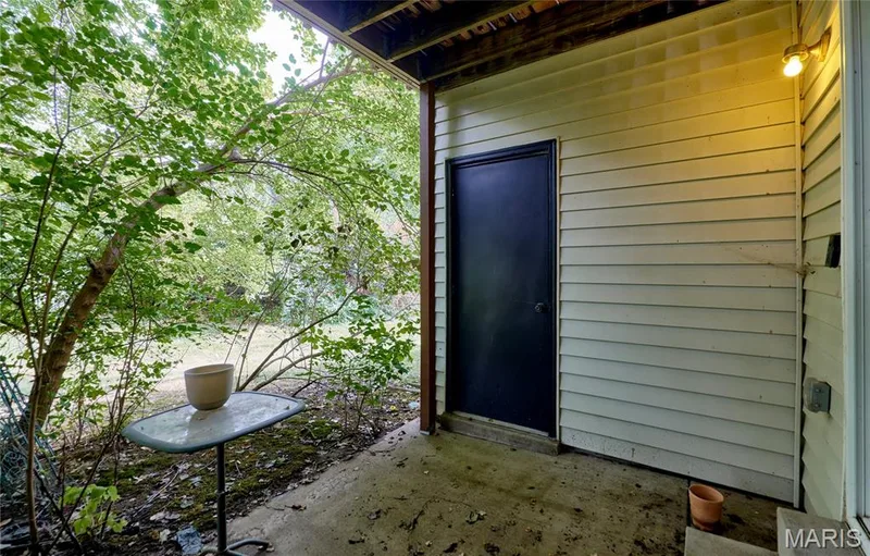 Rear covered patio with concrete flooring, accented by mature trees and a storage space — 146 Old Buggy Court #A, St Charles, MO 63304