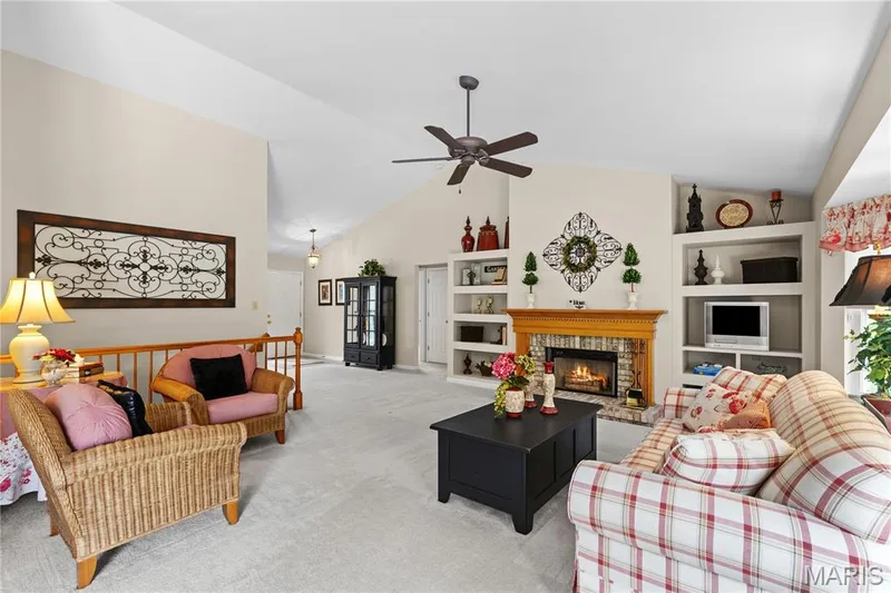 View of Vaulted great room showing lit fireplace, ceiling fan and bookcases — 8 Autumn Grove Court, O'Fallon, MO 63366