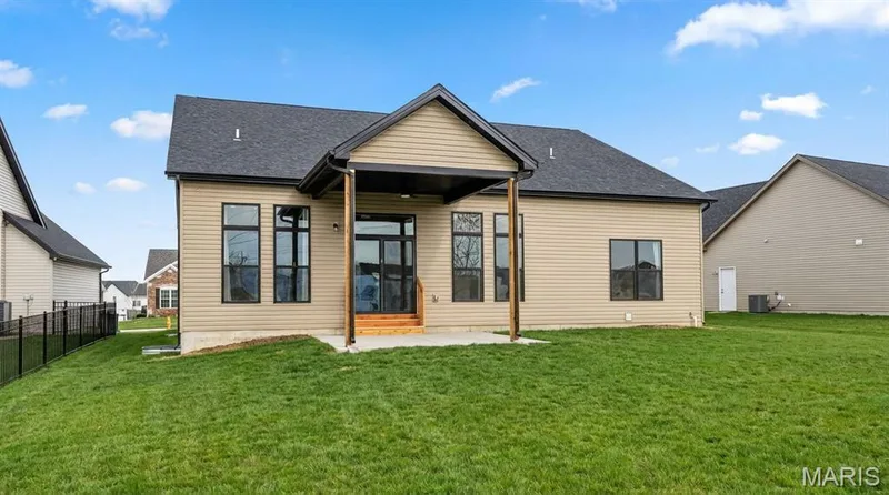 Expansive rear exterior featuring a covered patio, tan siding, and a dark shingle roof — 312 Summer Glen Lane, St Charles, MO 63301