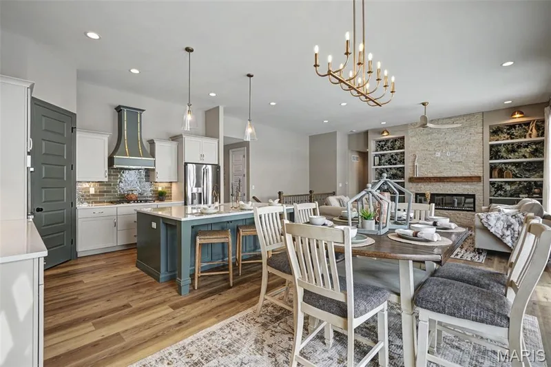 Open-concept living area featuring wood-finish flooring, a kitchen island with seating, a stone-clad fireplace, built-in shelving, and recessed lighting — 312 Summer Glen Lane, St Charles, MO 63301