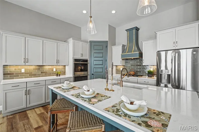 Kitchen featuring a large central island with seating, light-toned cabinetry, light wood-finish flooring, stainless steel appliances, and a distinct range hood — 312 Summer Glen Lane, St Charles, MO 63301