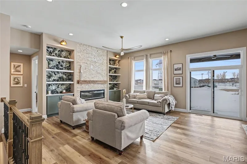 Spacious living area featuring wood-finish flooring, a stone-clad fireplace with a wood mantle, and built-in shelving with accent lighting — 312 Summer Glen Lane, St Charles, MO 63301