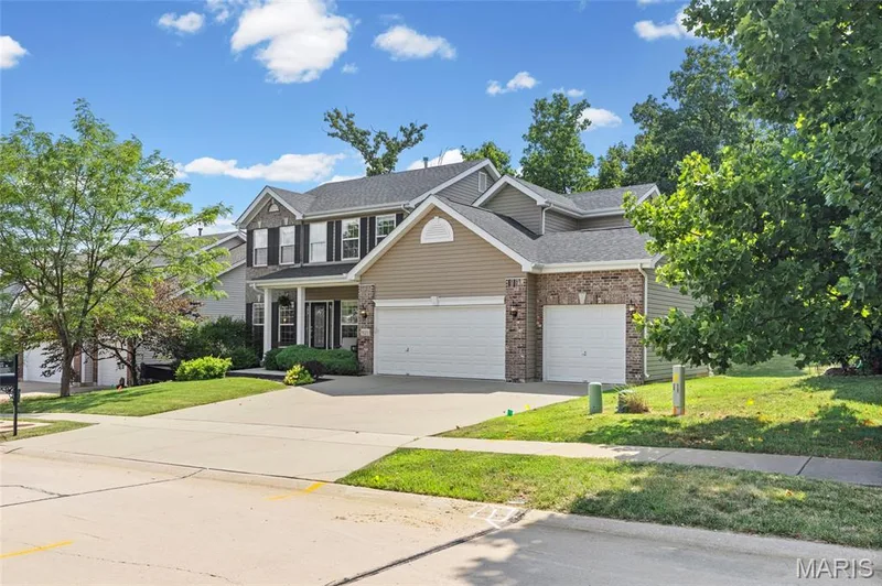 Two-story residence featuring a covered front porch with white columns, a three-car garage, and stone veneer accents — 921 Molloy Drive, O'Fallon, MO 63366