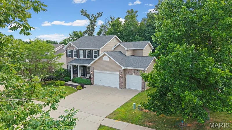 Two-story residence featuring a covered front porch with white columns, a three-car garage, and stone veneer accents — 921 Molloy Drive, O'Fallon, MO 63366