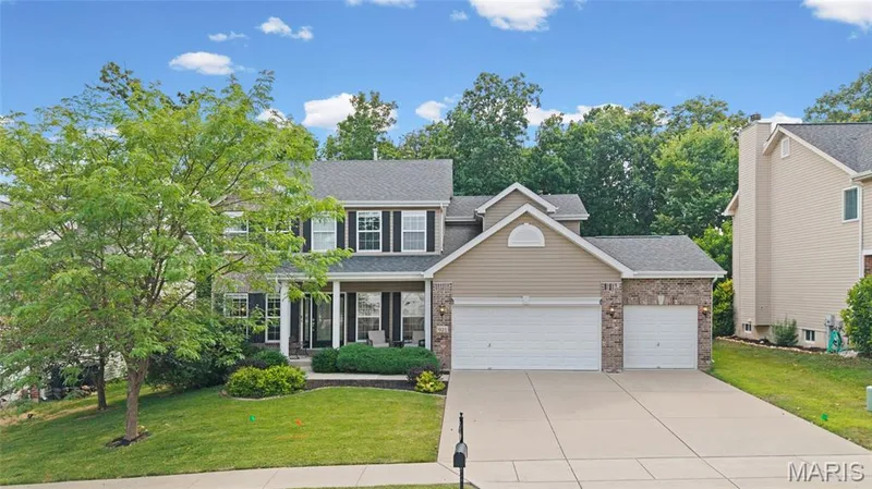 Two-story residence featuring a covered front porch with white columns, a three-car garage, and stone veneer accents — 921 Molloy Drive, O'Fallon, MO 63366