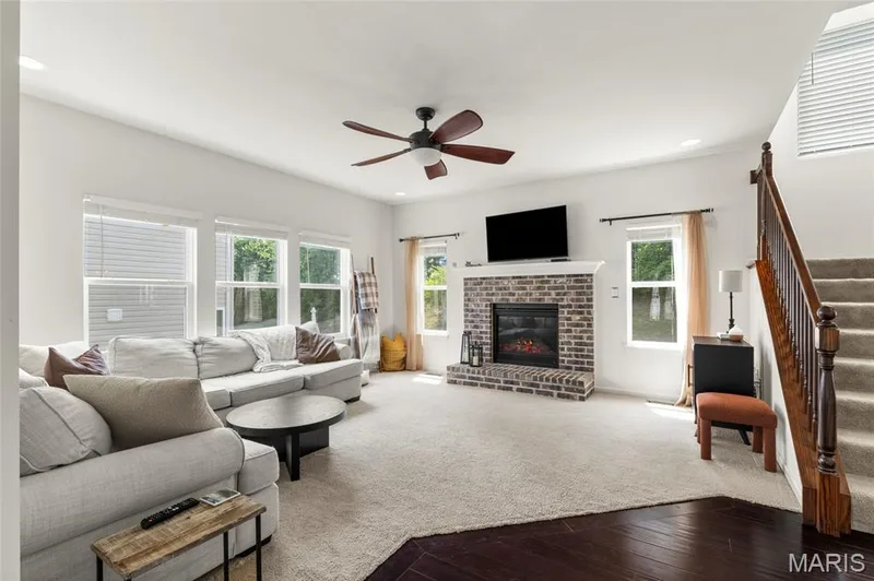 Spacious living area featuring a brick gas fireplace with a white mantel, ceiling fan, recessed lighting, multiple windows, staircase with carpeted to upstairs or basement. — 921 Molloy Drive, O'Fallon, MO 63366