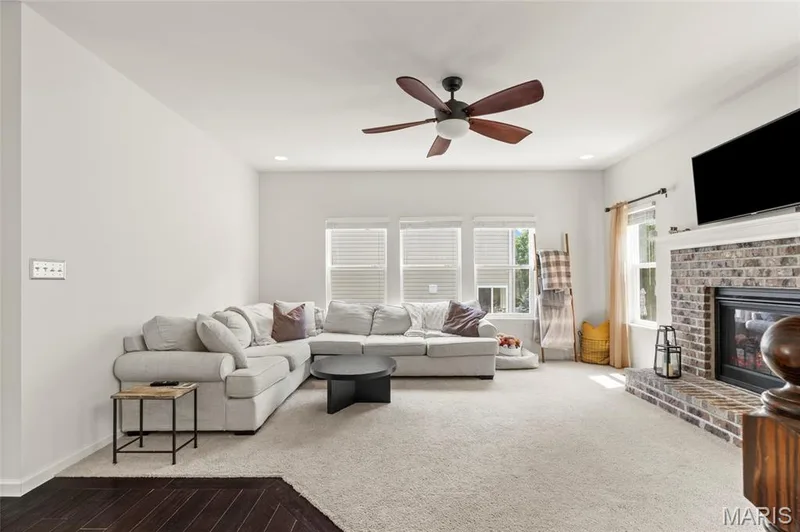 Living area featuring a brick gas fireplace, built-in television mount, wood-finish ceiling fan, recessed lighting, and multiple windows with blinds — 921 Molloy Drive, O'Fallon, MO 63366