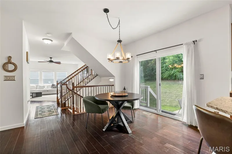 Wood-finish flooring throughout, featuring a staircase with wood balusters and handrail, a contemporary chandelier, and a sliding glass door leading to the backyard. — 921 Molloy Drive, O'Fallon, MO 63366