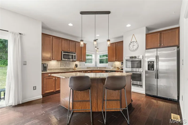 Kitchen featuring a central island with granite countertop, wood-finish cabinetry, stainless steel appliances, and dark wood-finish flooring — 921 Molloy Drive, O'Fallon, MO 63366