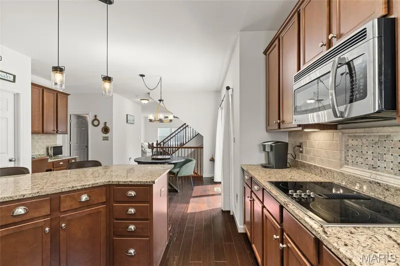 Kitchen featuring wood-finish flooring, wood cabinetry, stone countertops, and a tile backsplash — 921 Molloy Drive, O'Fallon, MO 63366