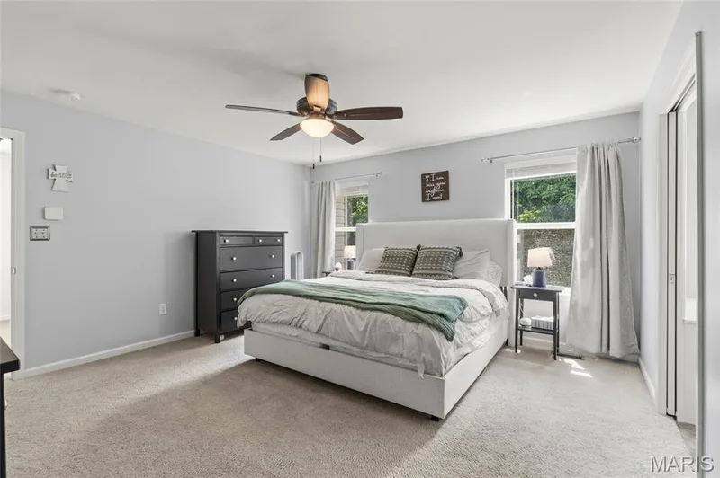Spacious primary suite featuring light gray walls, plush carpet flooring, two windows, and a ceiling fan with integrated lighting. Walk-in closet with organizers and a bath with a separate tub, shower, and double vanity. — 921 Molloy Drive, O'Fallon, MO 63366