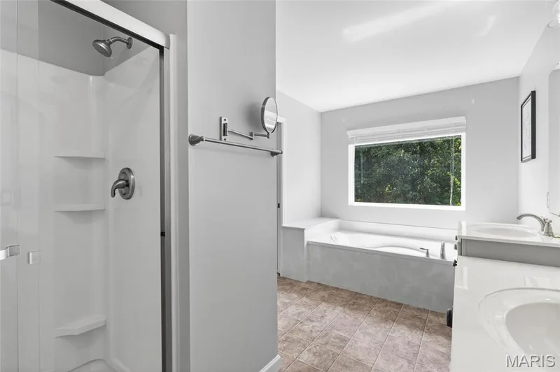 Primary Suite  featuring a walk-in shower with a glass enclosure, a built-in tub with surrounding ledge, dual vanity sinks with white countertops, and tile flooring — 921 Molloy Drive, O'Fallon, MO 63366